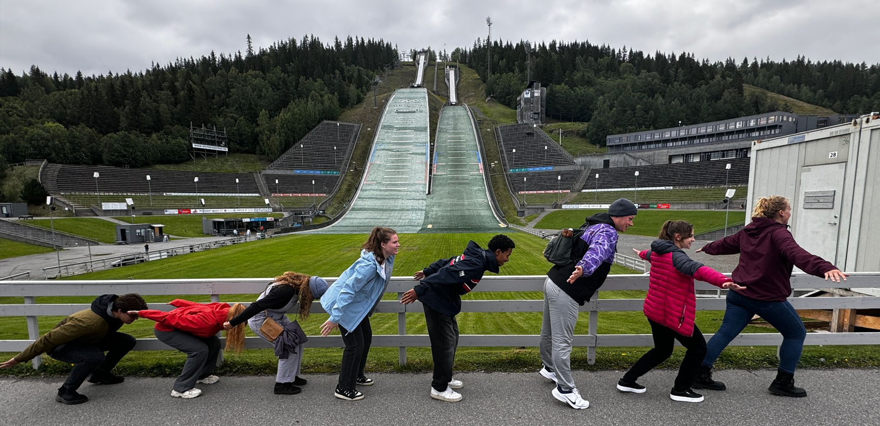 Exchange students standing in front of the ski jump in a row, pretending to be each step of jumping process. 