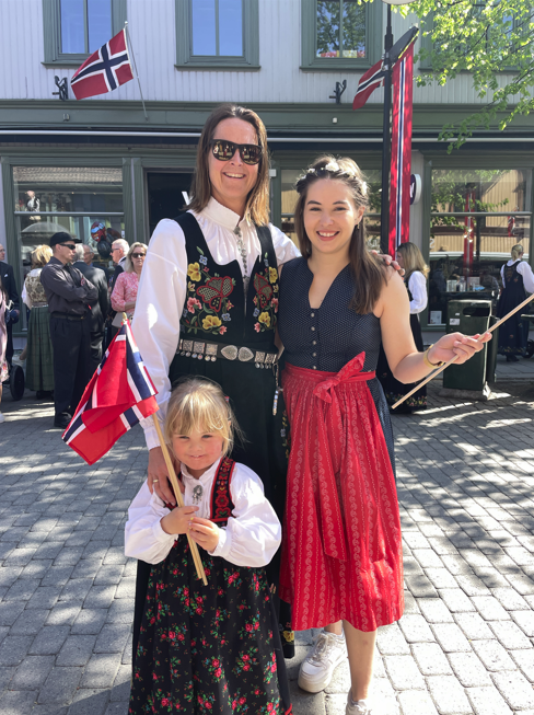 Exchang student posing with a Norwegian famly that is dressed in Bunad during the Norwegian Constitution Day, waving Norwegian flags.