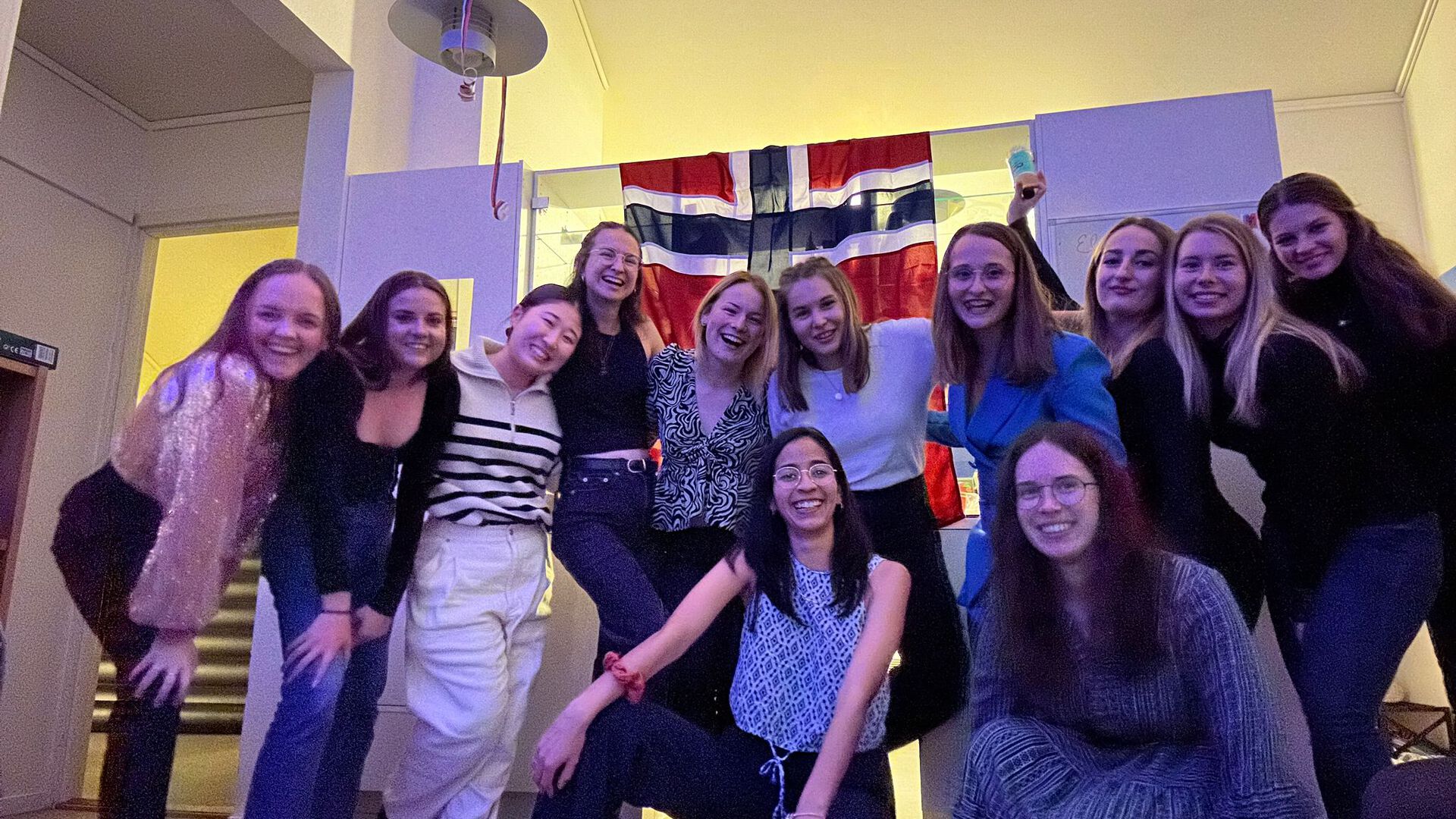 Elisa posing with international and local students in one of the dorms, with a Norwegian flag in the background.