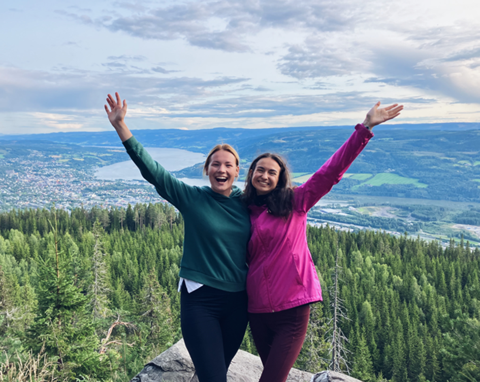 Kristine and her friend posing happily after hiking up the mountain Balbergkampen, with a view of Lillehammer in the background.