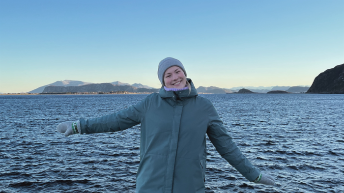 Kristine posing happily in front of the ocean, dressed in warm clothes.