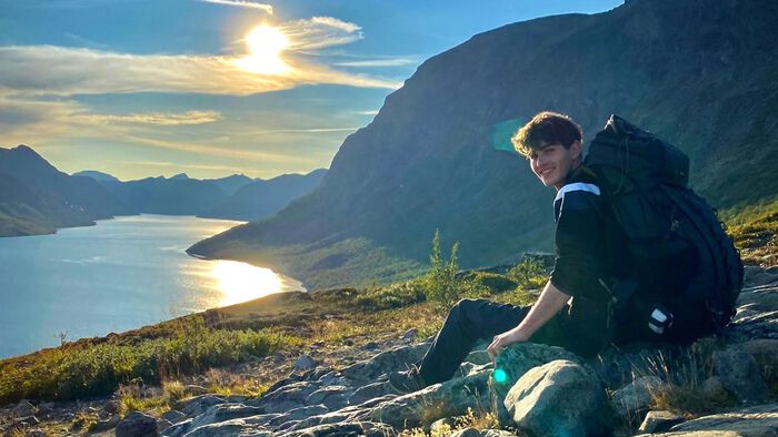 Sacha is sitting on a muntain top in the sun. He is smiling
