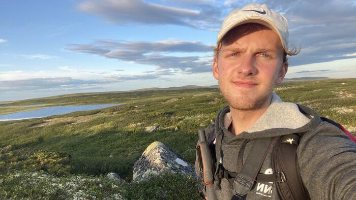 Exchange student taking a selfie on top of a moss covered mountain with blue sky