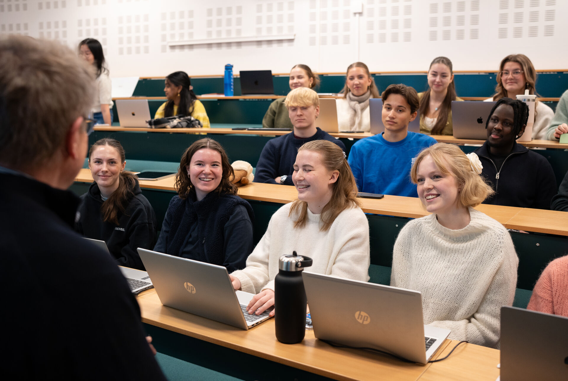 Students sitting in an auditorium during a lecture taking notes on their computers and paying attentiton to the professor.