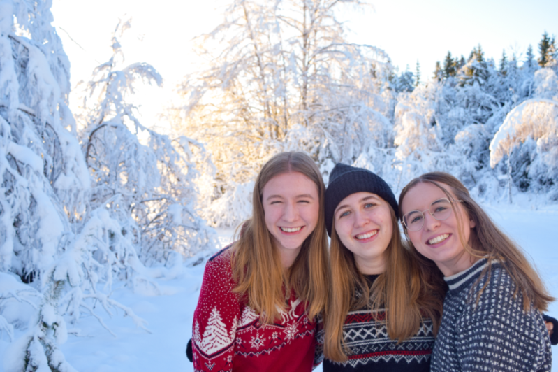 Female students posing happily in the snow covered forest, in Norwegian traditional knitted sweathers.