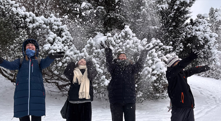 Students throwing snow upwards happily while dressed in warm winter clothes