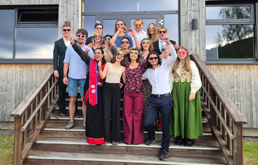 Students smiling and laughing in sunglasses while posing for the camera on wooden steps outside dressed nicely while celebrating their graduation.