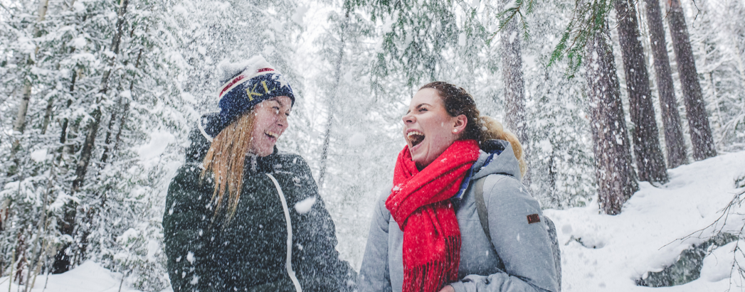Female students standing in the middle of the snow-covered forest with winter clothes, laughing and having fun with snow falling.