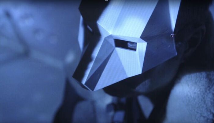 Person in a stylized cardboard wolf mask in a blue light.