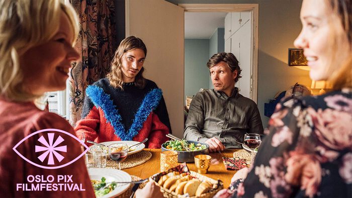 Bilde fra film hvor to kvinner i forgrunnen ser ivrig på hverandre mens to menn på andre siden av bordet ser skeptiske ut.