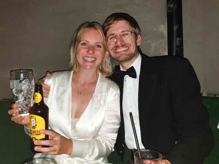 Produsent Tøri Gjendal i hvit festkjole skåler mot kamera sittende sammen med en festkledd regissør Iain Forbes i kilt sitter sammen og begge stråler.