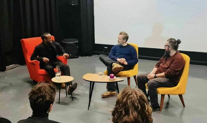 Hamza Kader sitter på scenen i samtale med regissører Pål Sletaune og Izer Aliu.