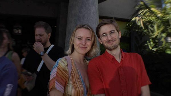 Produsent Tøri og regissør Iain står smilende sammen utendørs med en bygning og mennesker i bakgrunnen