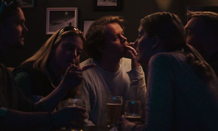 Bilde fra filmen Superdupermegagigasingel hvor en ung mann sitter på bar omgitt av to jenter og to gutter mens han ser undrende ut i luften.