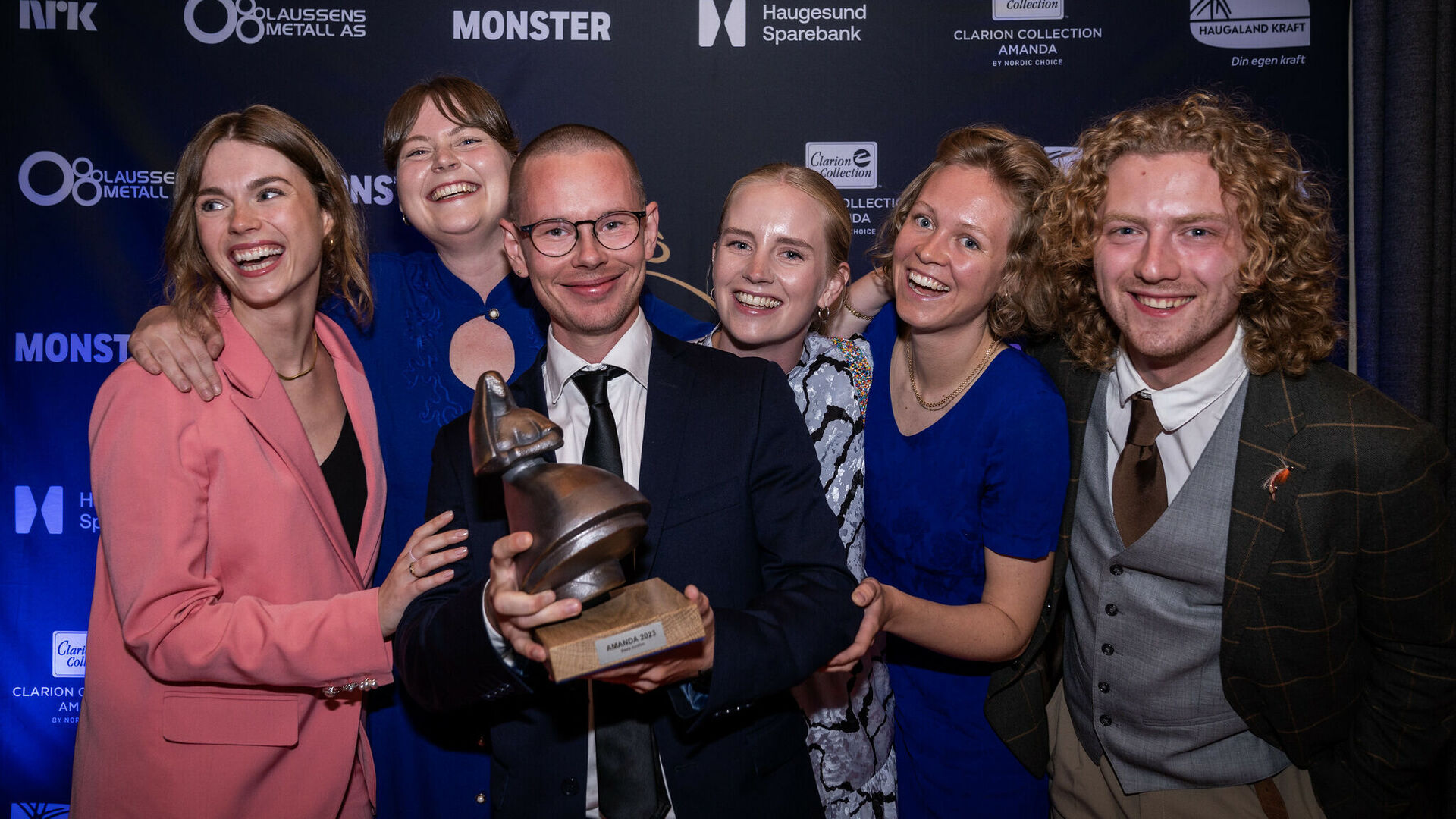 Et festkledd filmteam med fem filmskolealumni poserer strålende samlet rund regisssøren som Amandastatuetten i armene.