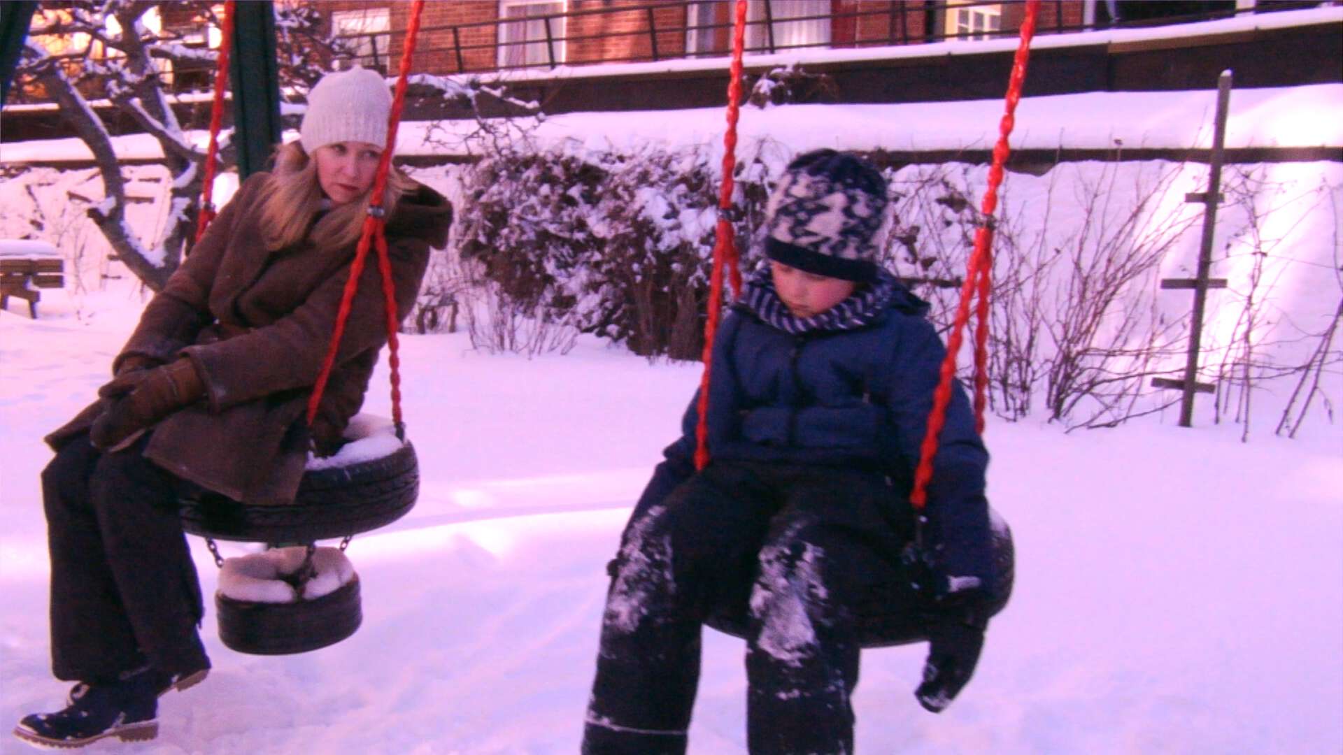 En mor og sønn sitter alvorlige på hver si huske i snøen.