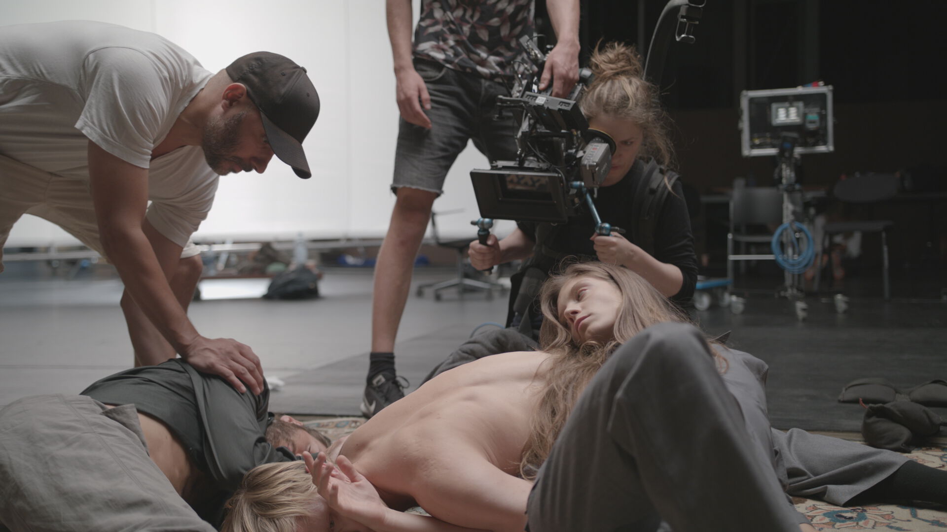 En fotograf filmer dansere som ligger omslynget på gulvet i et studio.