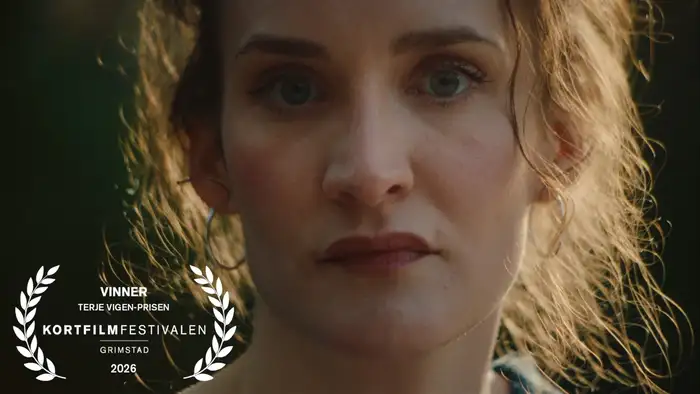 Still fra filmen "Hildring", et nærbilde av en kvinne med lett bekymret uttrykk med løst oppsatt hår opplyst av sollys bakfra.