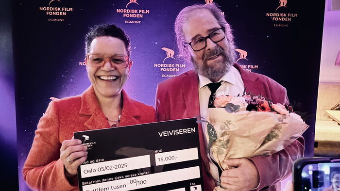 Glade prismottakere, faglig leder på Filmskolen Eli Bø og Filmskolens først dekan Malte Wadman smiler med blomster og holder en stor sjekk på 75 000 kroner for prisen Veiviserenforan seg
