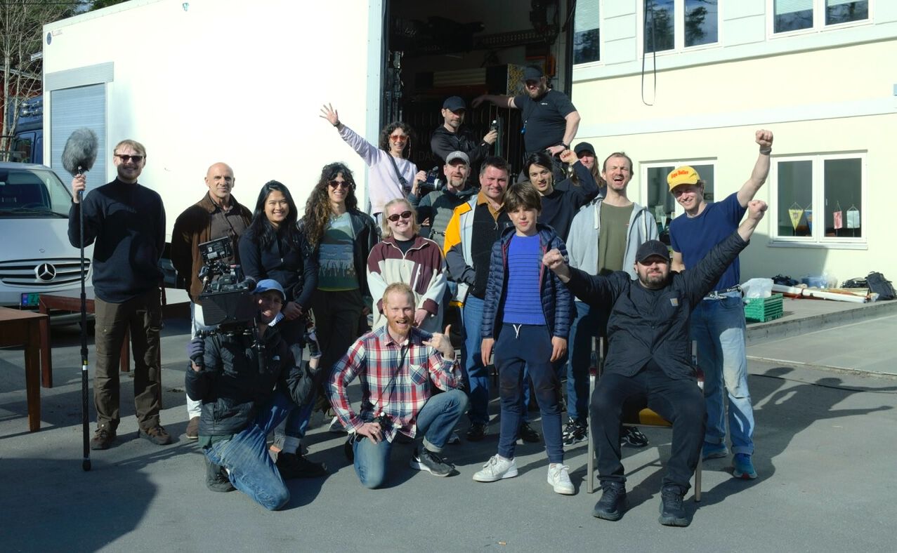 Gruppebilde av et oppstilt jublende filmcrew på 18 personer.