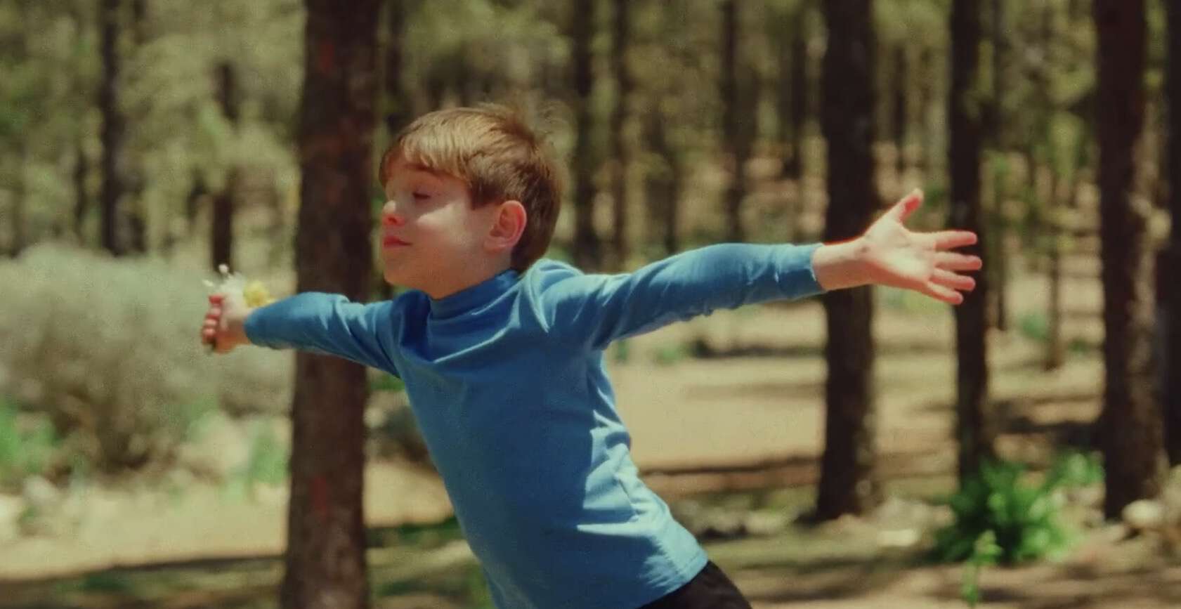 En liten gutt løper med armene utstrakt i en solfylt skog. Øynene er lukket, på ansiktsuttrykket ser han nesten ut som han svever gjennom skogen.