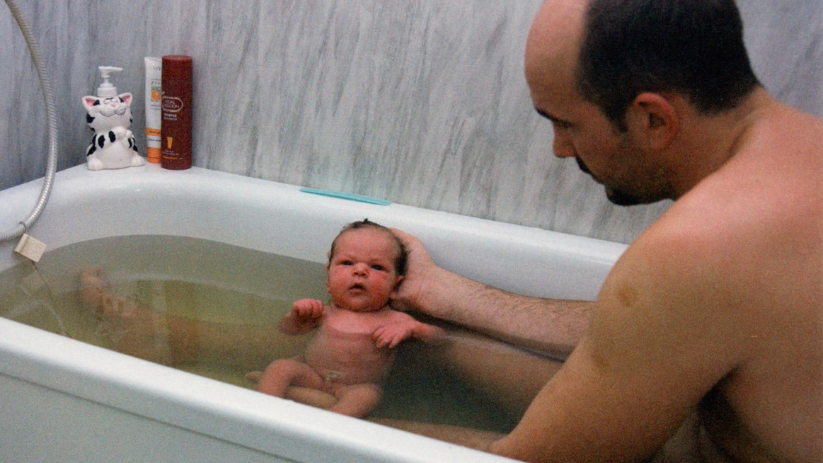 Far sitter i badekar med baby som han holder varsomt.