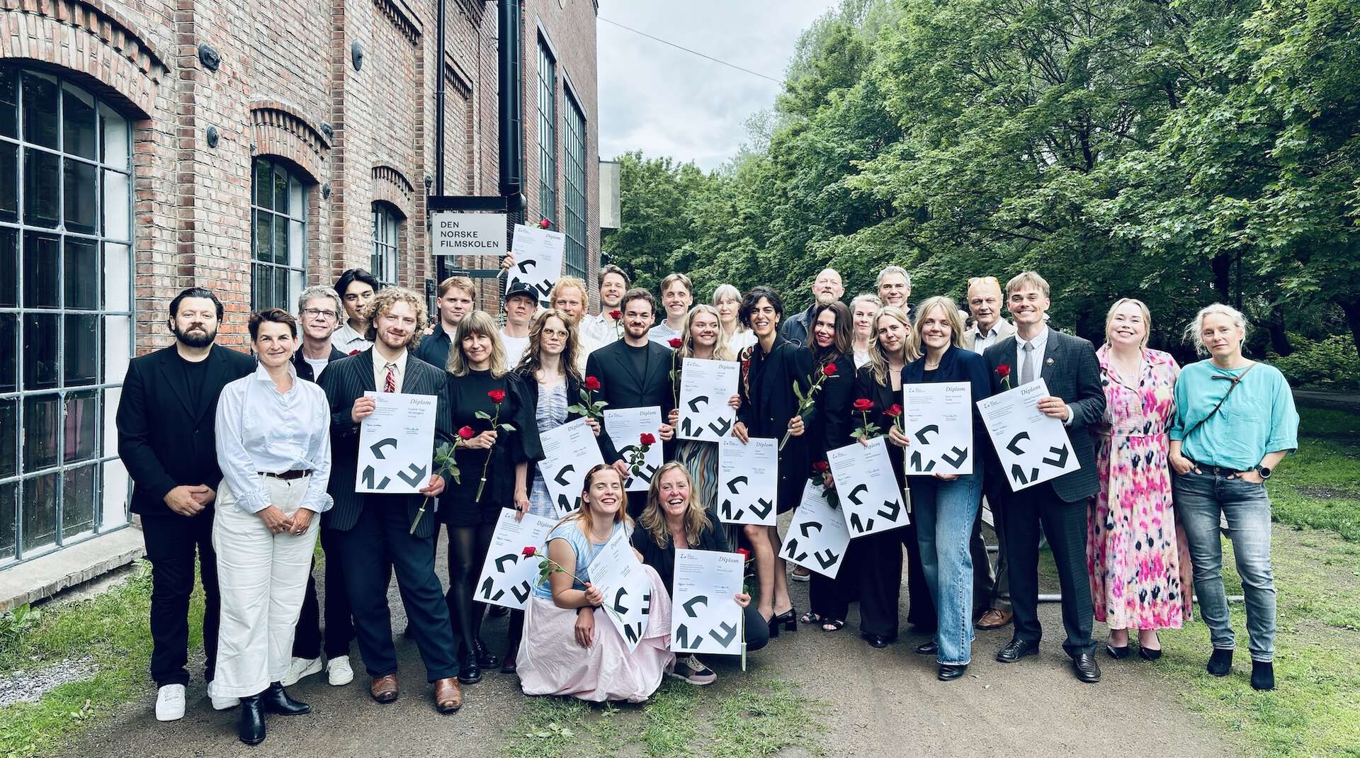 Glad gjeng med 20 studenter står oppstilt ute med diplomer og roser i hendene sammen med lærerne .