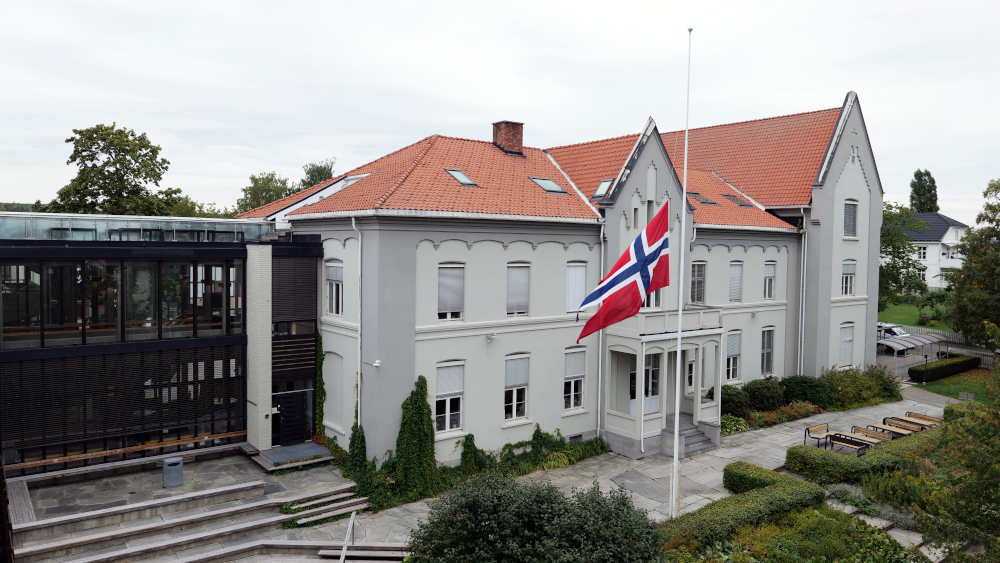 En flaggstang med et norsk flagg på halv stang foran hovedbygget ved studiested Hamar