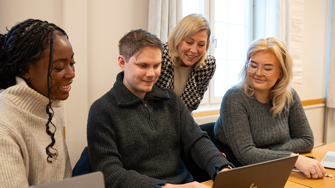 Tre smilende studenter og en foreleser. 