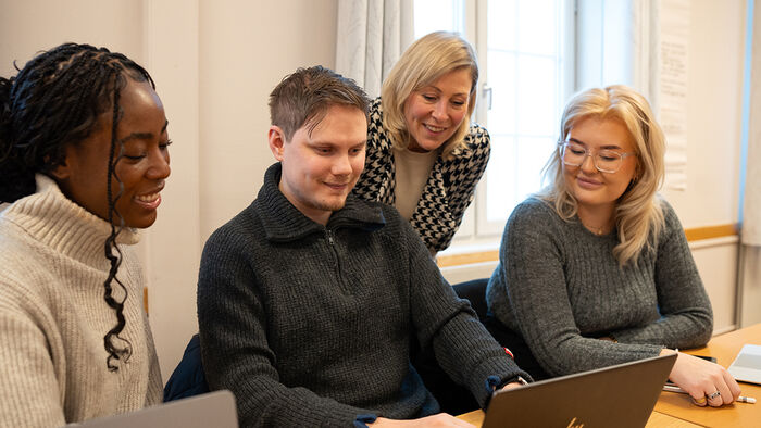 Tre smilende studenter og en foreleser. 