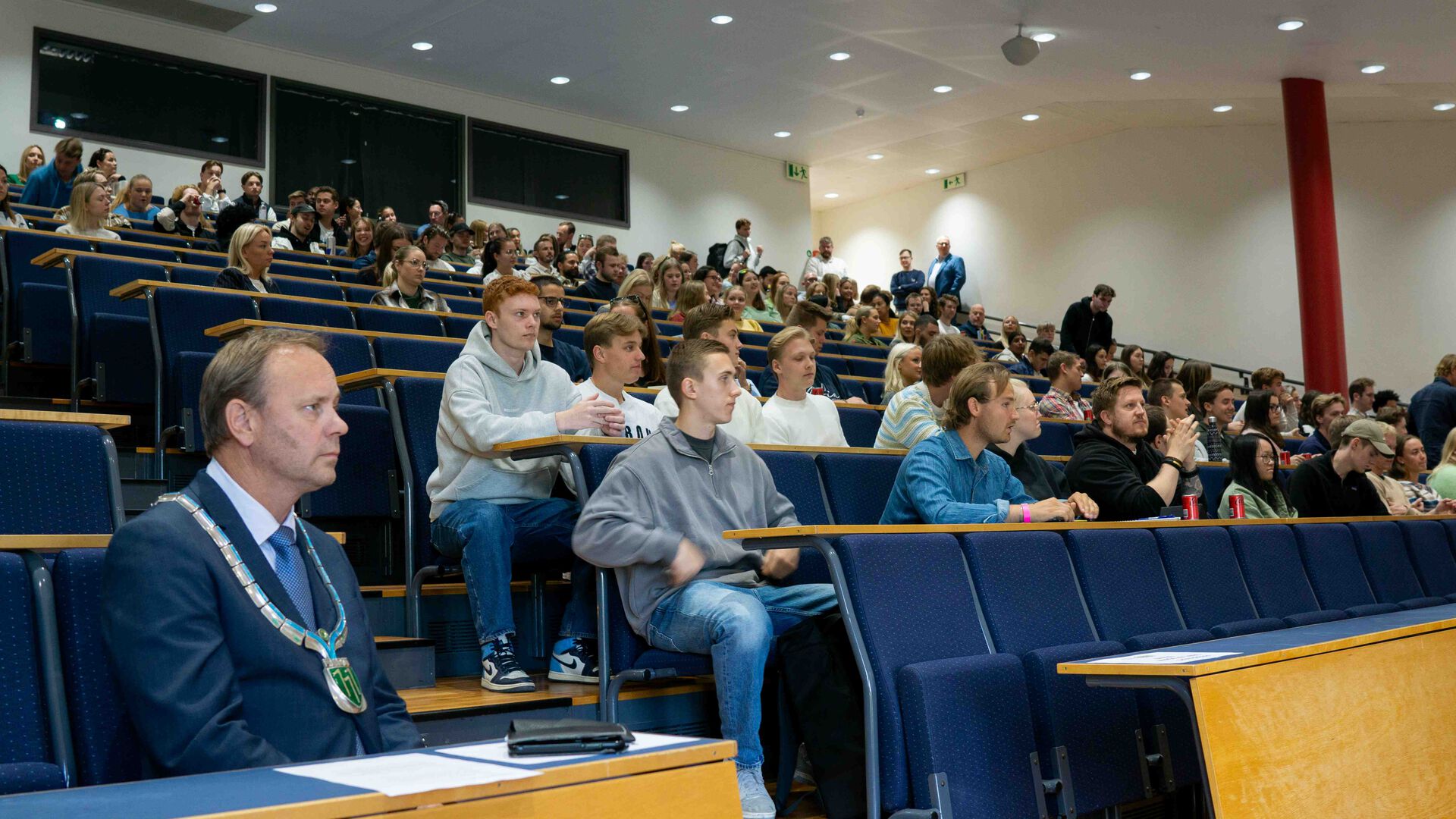 Auditorium med mange studenter, ordfører med ordførerkjedet foran.