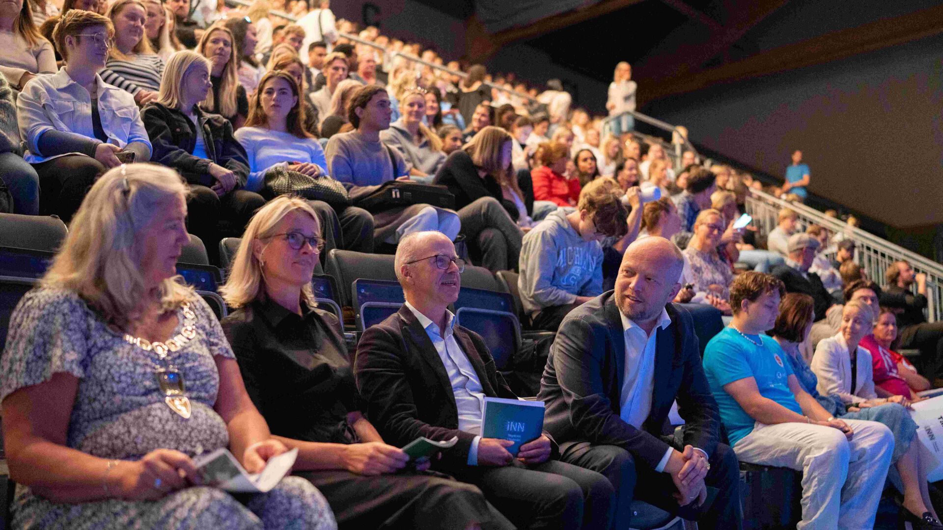 Studenter sitter på tribunen inne i idrettshallen på terningen Arena. Ordfører, prodekan utdanning, dekan og finansminister på første rad.