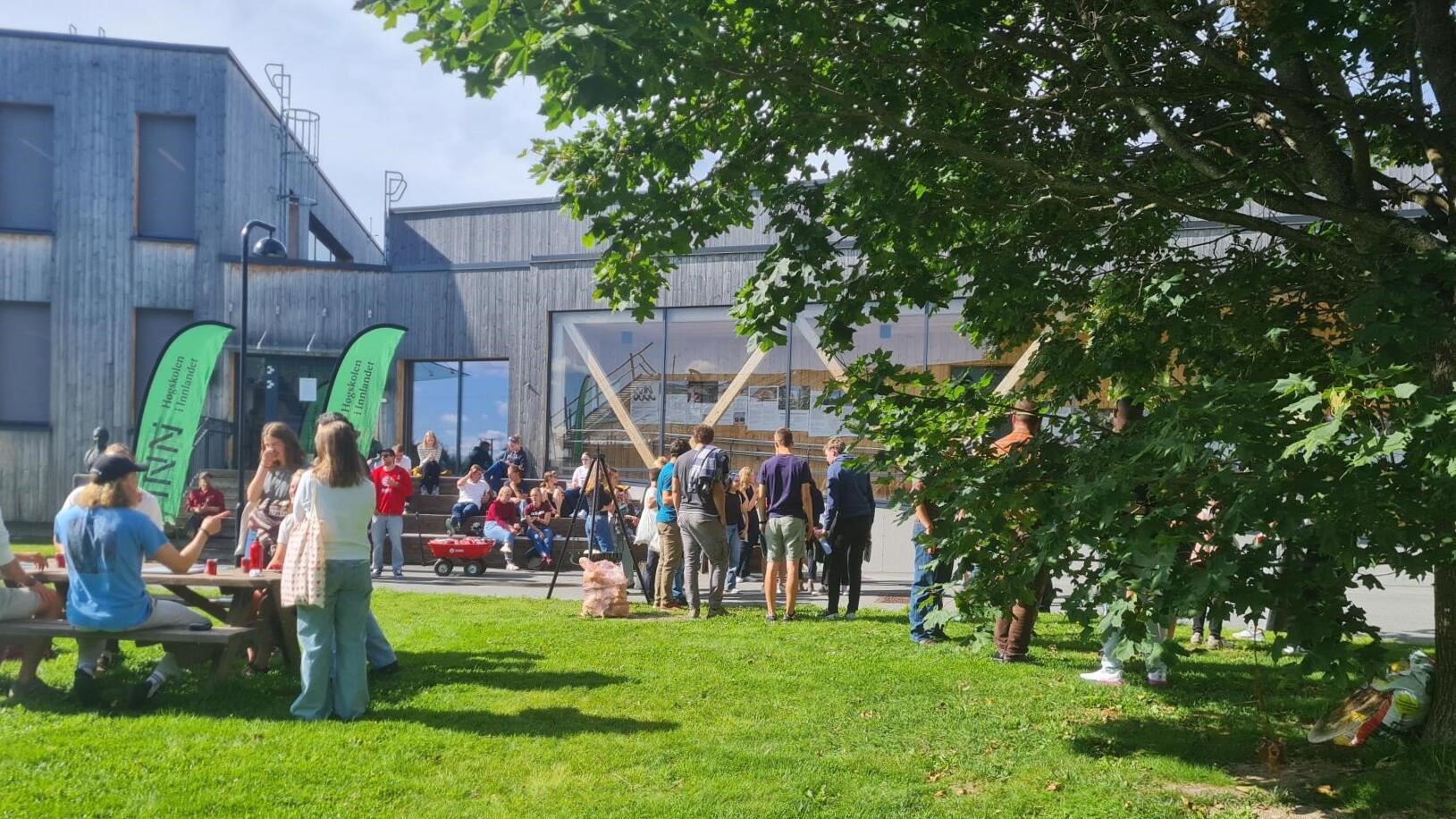  Utebilde fra Evenstad, blå himmel, grønt gress en sølvfarget elgstatue og studenter