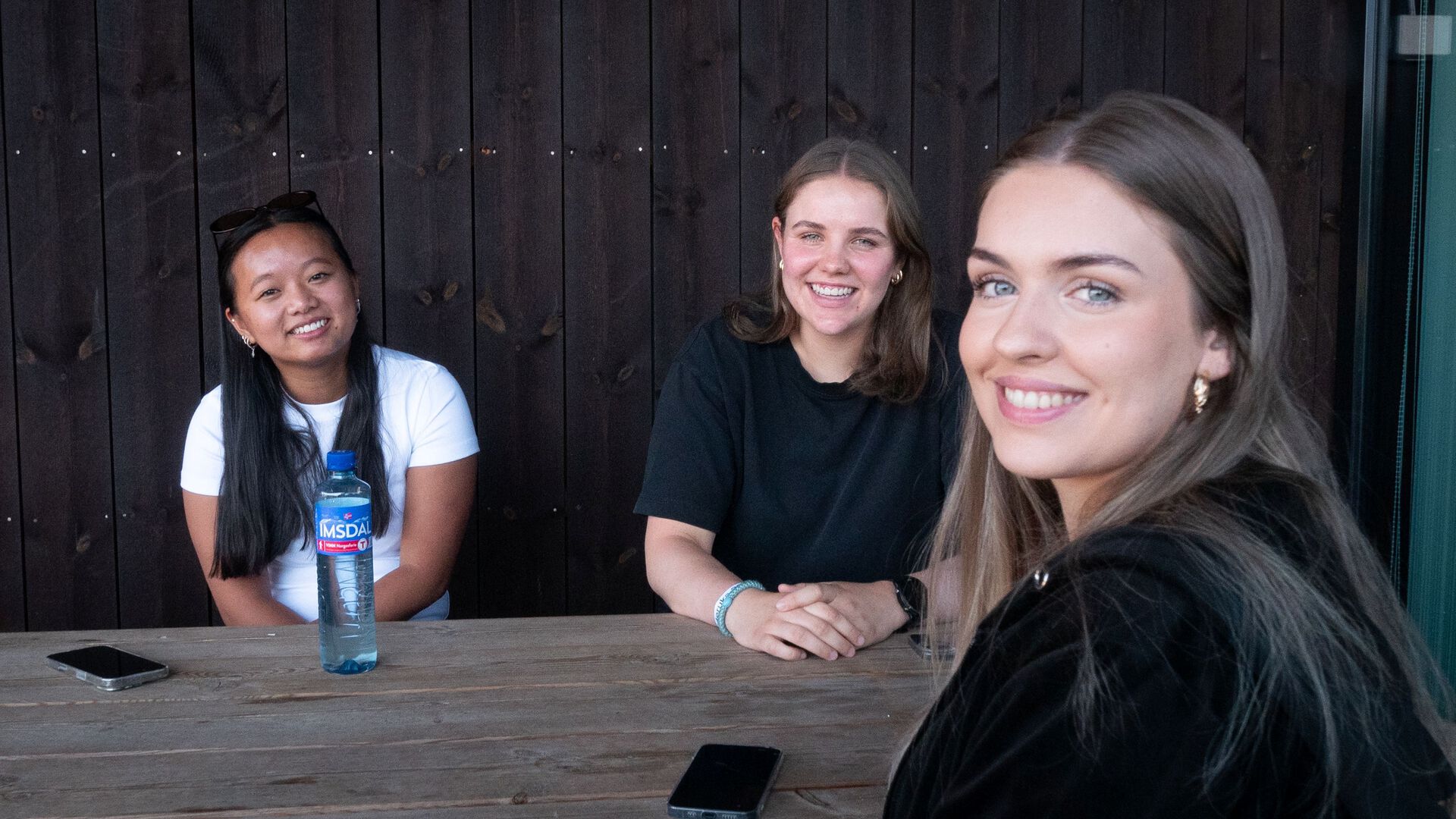 Tre stduenter sitter ute på Elverum, ser i kamera og smiler.