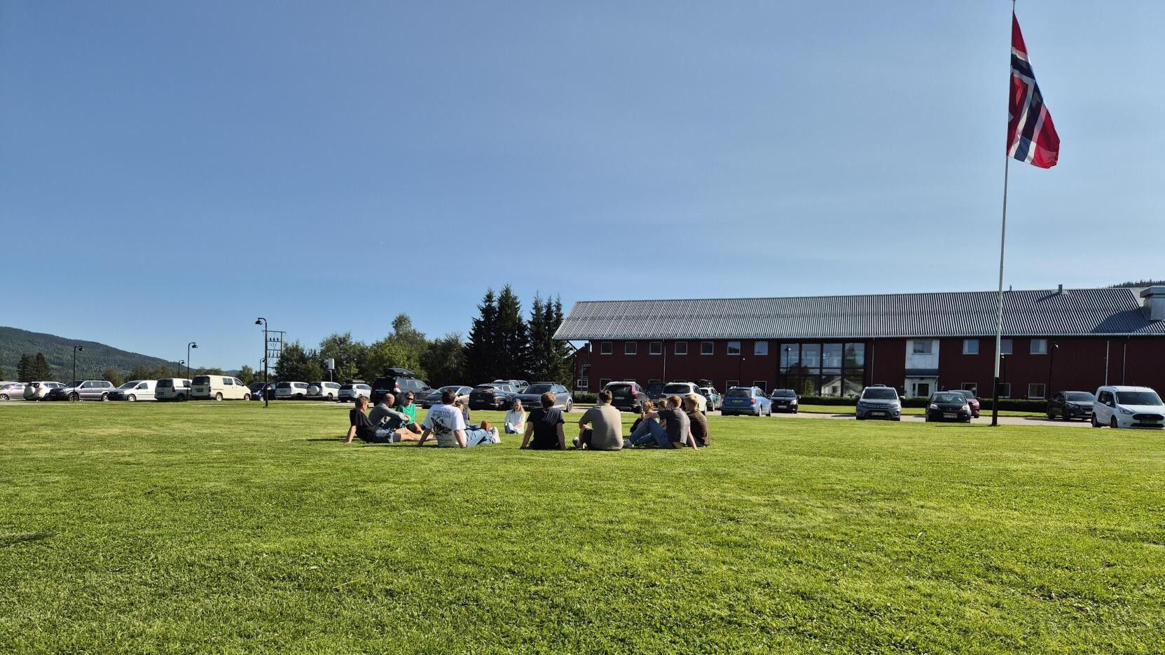 Oversiktsbilde ute Evenstad studenter sitter på gressplenen flagget til topps