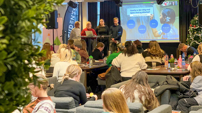 Bilde av tre studenter på en scene foran folk og med skjem bak seg