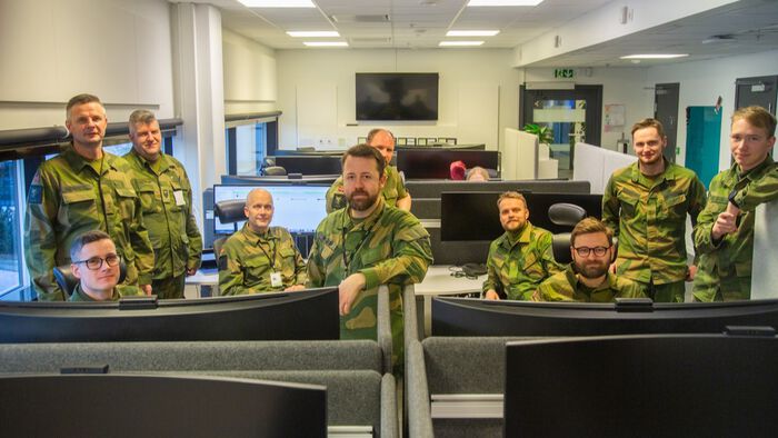 11 menn i Heimevernsuniform inne i et kontorlandskap