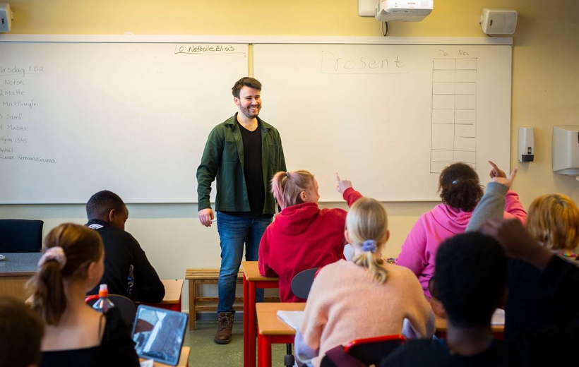 En lærer som står foran elever i et klasserom som sitter med ryggen til