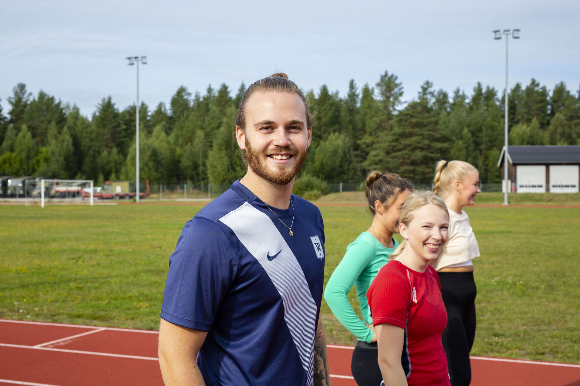 En mannlig og tre kvinnelige studenter på idrettsplass. Den mannlige studenten ser rett i kamera.