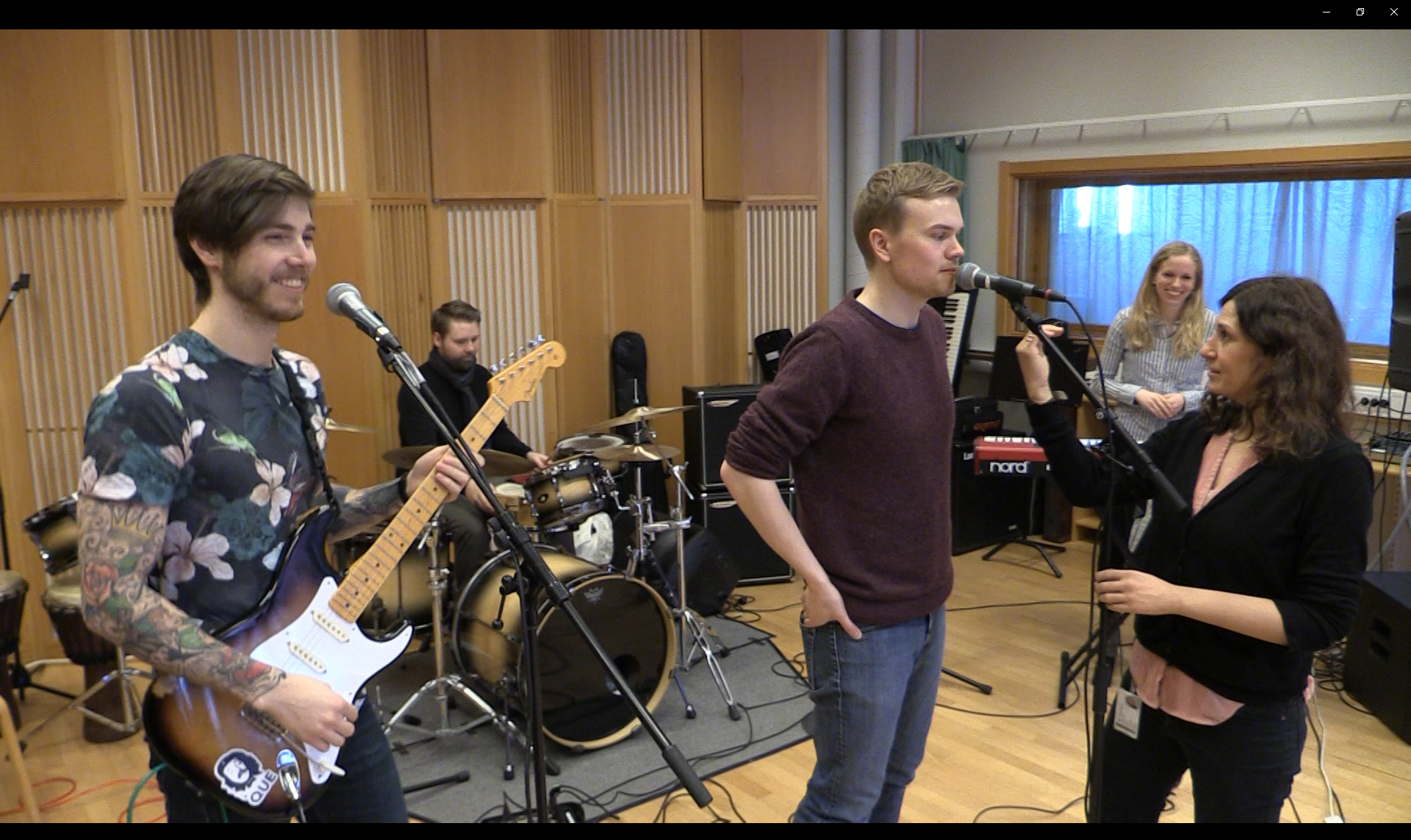 Bilde av et band av studenter i musikksal som får instruksjoner av lærer.