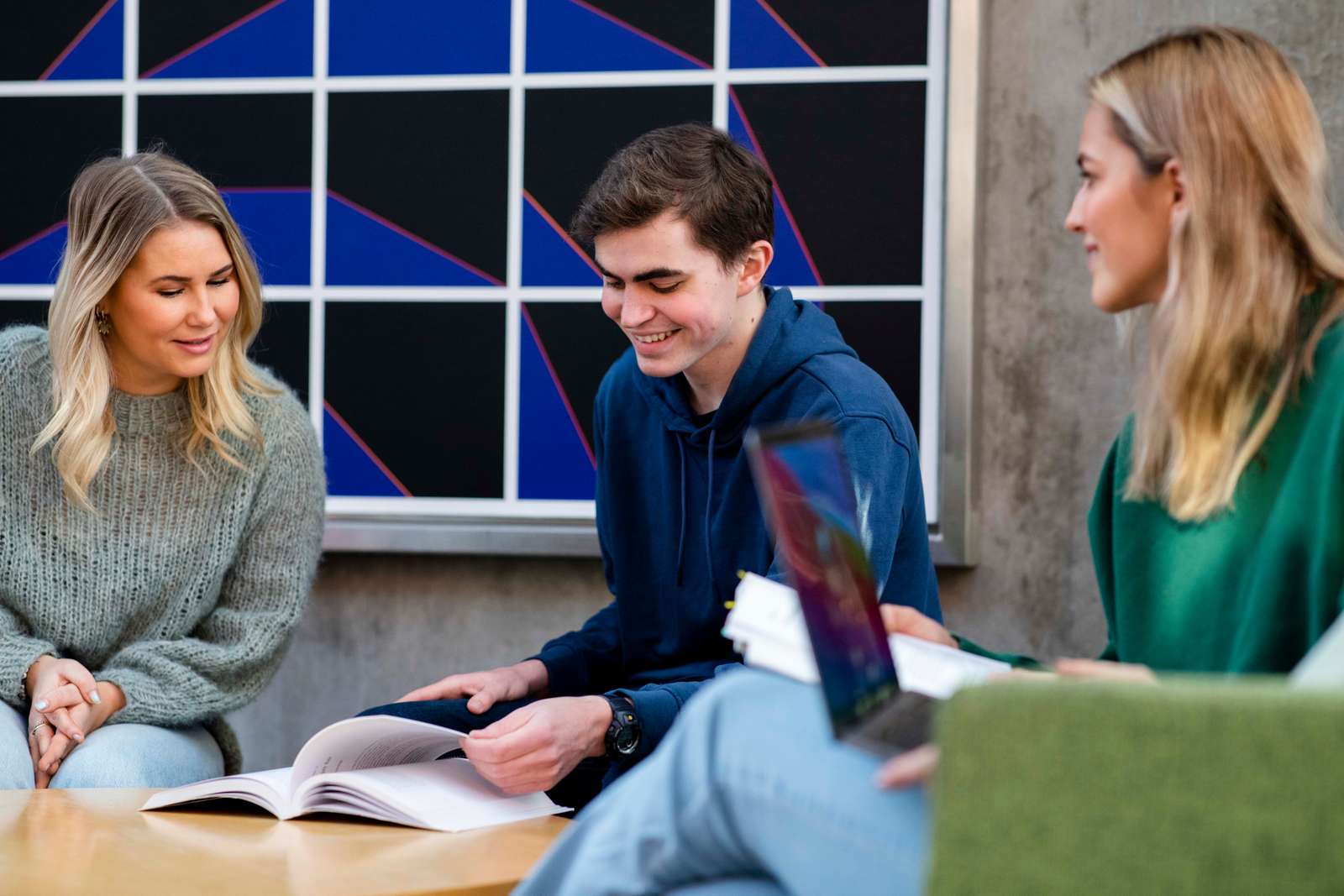 Tre studenter i samtale i gruppearbeid. Gutten i midten blar i en bok.