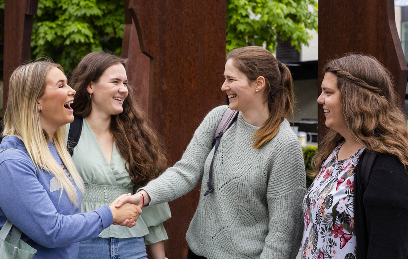 Fire muntre kvinnelige studenter i samtale, to av dem håndhilser.