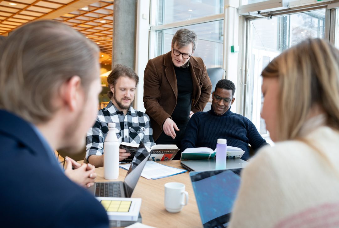 Lærer veileder studenter som sitter rundt et bord.