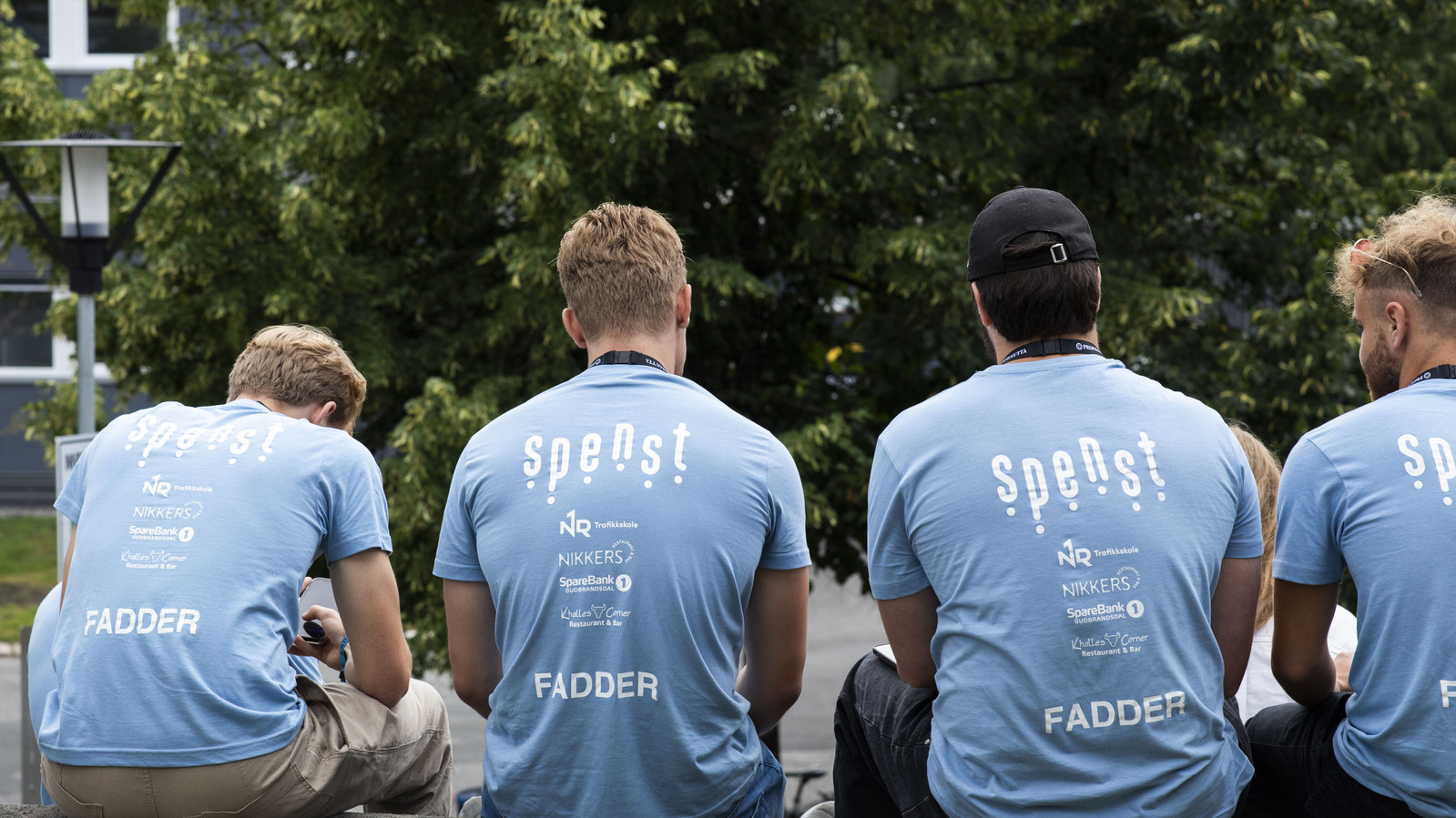 Ryggen til fire studenter som har på seg lyseblå fadder t-skjorter