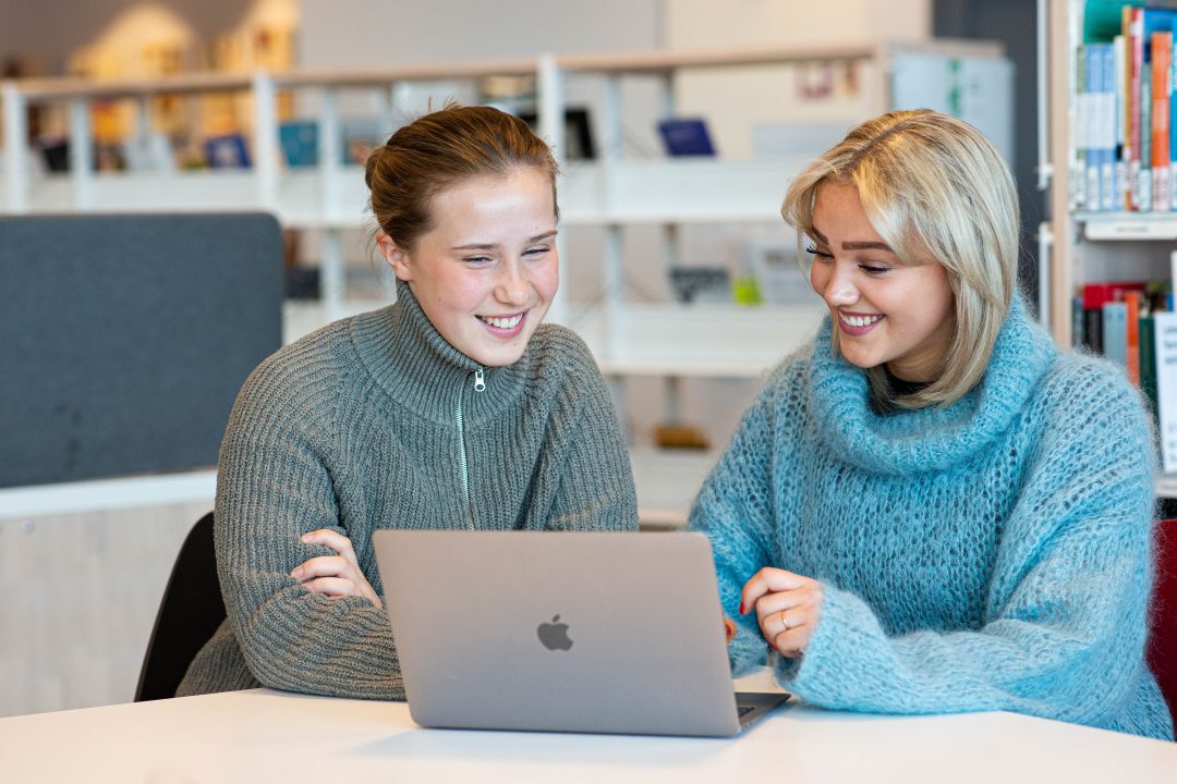 To jenter som sitter å ser på en mac.