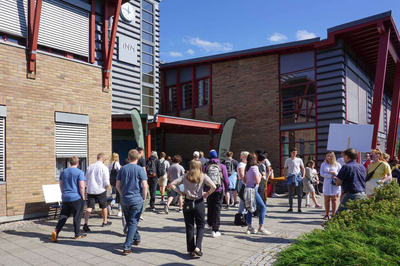 Studenter ved studiestart utenfor bygg på Rena. Blå himmel og det ser varmt ut.
