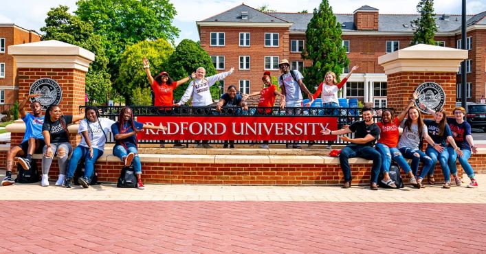 Students sitting next to and standing behind the Radford University sign. They greet you welcome.