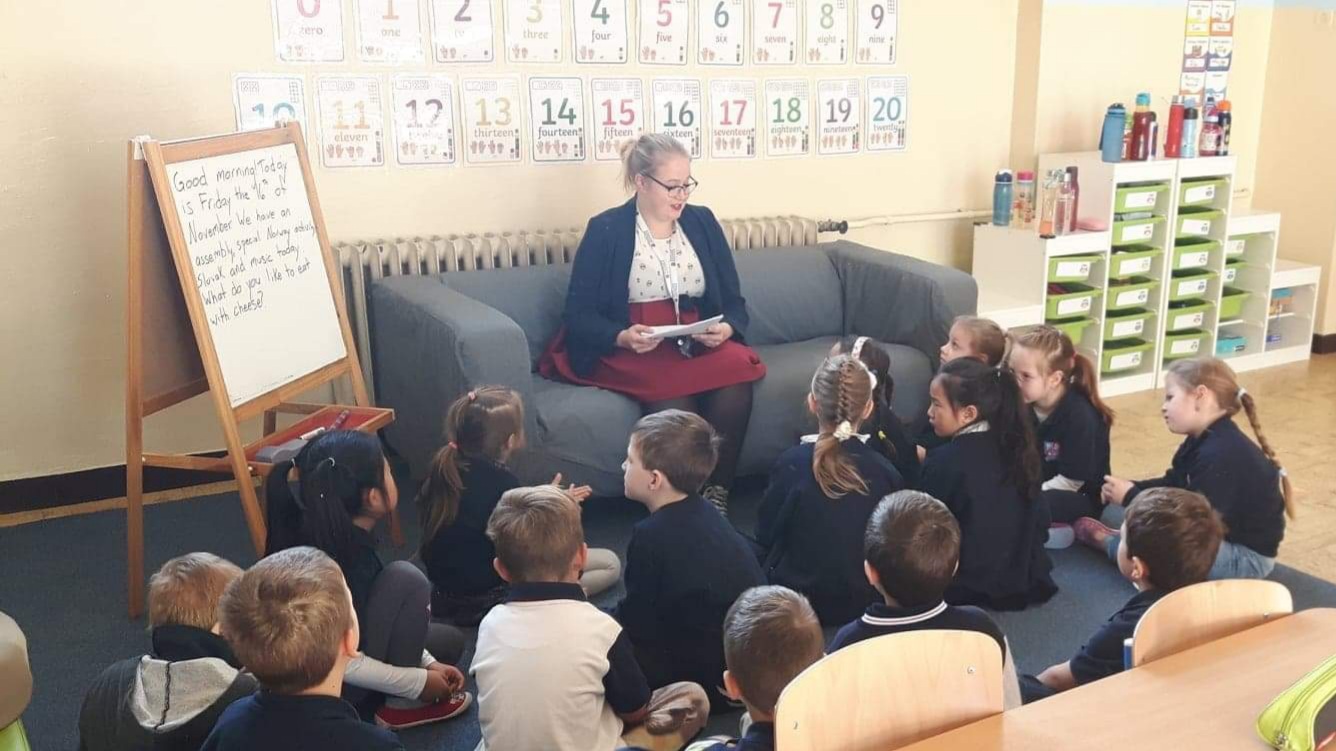 Student reading from a book in front of kindergartners