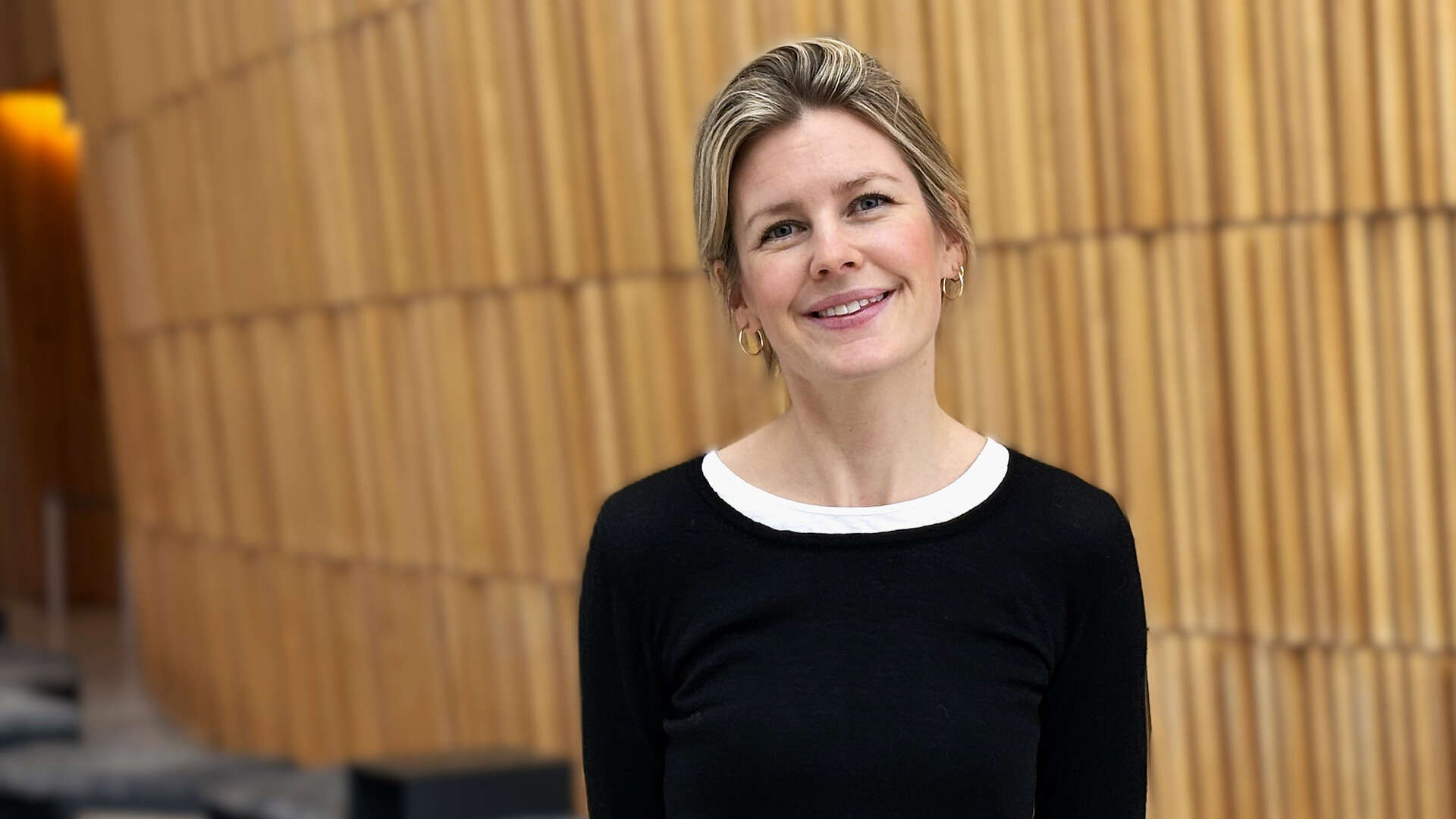 Portrettbilde av en ung dame med svart genser mot en trevegg