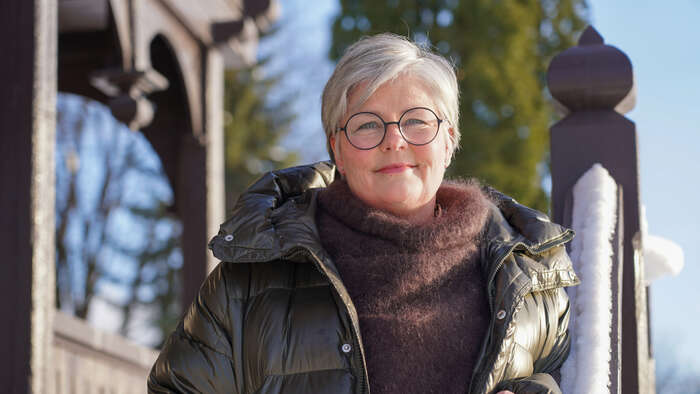 Dame på trappa til et stabbur om vinteren med boblejakke og skjerf